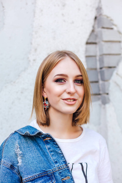 Fashion girl standing near brick wall in denim oversized jacket and beautiful ear rings. - Fotoğraf, Görsel
