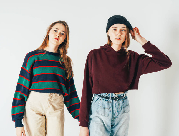 Kaksi siskoa kaksoset kauniita tyttöjä hipsterit rento vaatteet katso kamera harmaalla taustalla eristetty
 - Valokuva, kuva