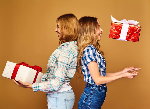 Christmas, x-mas, concept.Two smiling beautiful women in stylish clothes.Girls posing on golden background.Models with big gift boxes.Having fun,ready for celebration.Bright holiday of best friends - Zdjęcie, obraz