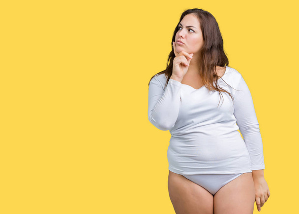 Beautiful plus size young overwight woman wearing white underwear over isolated background with hand on chin thinking about question, pensive expression. Smiling with thoughtful face. Doubt concept. - Fotoğraf, Görsel