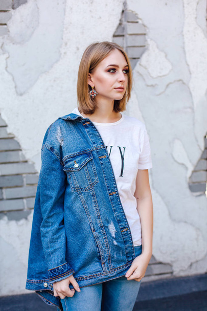 Fashion girl standing near brick wall in denim oversized jacket and beautiful ear rings. - Photo, image