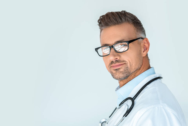 portrait of handsome doctor in glasses with stethoscope on shoulders looking at camera isolated on white - 写真・画像