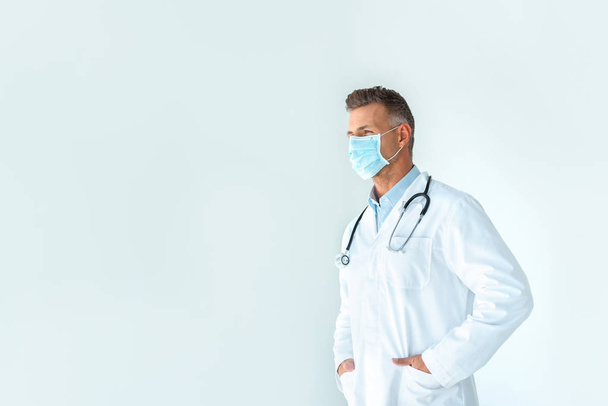 handsome doctor in white coat and medical mask looking away isolated on white - Foto, Imagen
