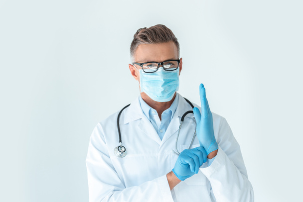 handsome doctor in medical mask wearing latex gloves and looking at camera isolated on white - Valokuva, kuva