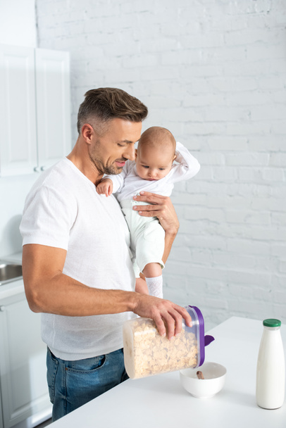 father holding baby daughter and preparing breakfast in kitchen  - Foto, Imagem