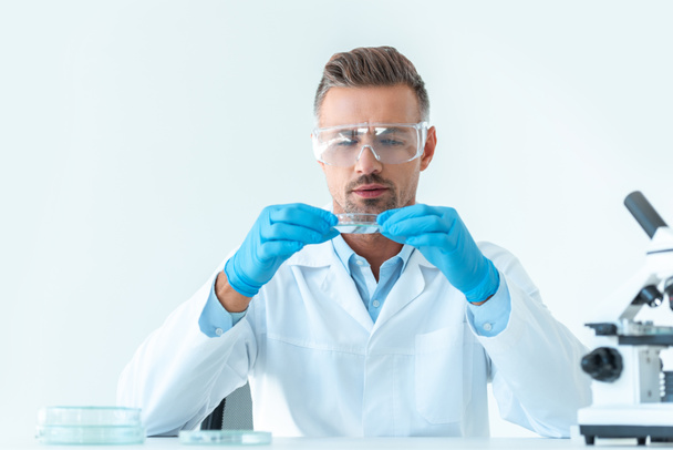 handsome scientist in protective glasses looking at reagent during experiment isolated on white - Foto, Imagen