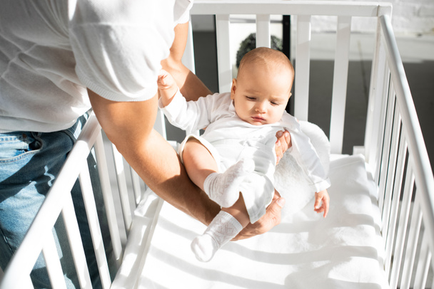 cropped view of father putting infant daughter into baby crib  - Fotoğraf, Görsel