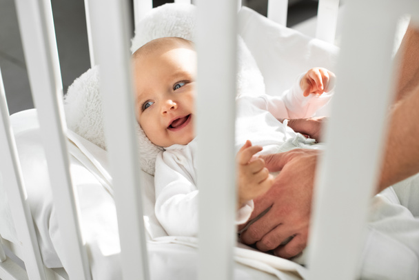 recortado vista de papá poniendo alegre bebé en bebé cuna
  - Foto, Imagen