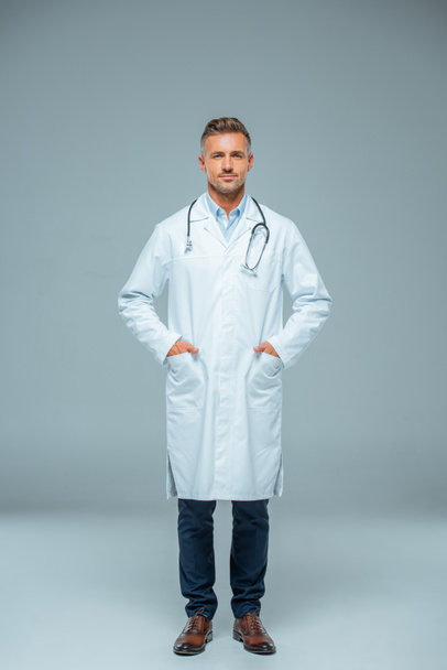 handsome doctor with stethoscope looking at camera on grey - Photo, Image