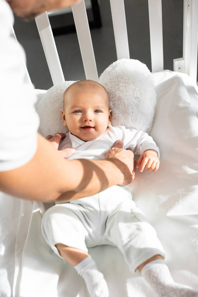 recortado vista de padre poniendo alegre bebé en bebé cuna
  - Foto, Imagen