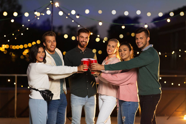 friends clinking party cups on rooftop at night - Photo, Image