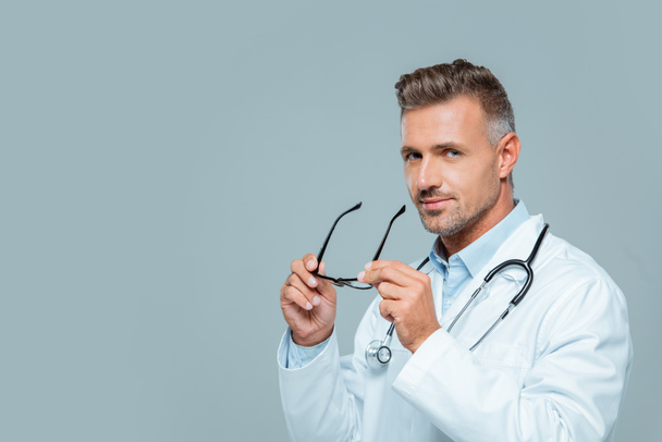 bel medico con stetoscopio tenendo gli occhiali e guardando la fotocamera isolata su bianco
 - Foto, immagini