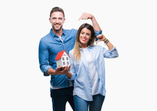 Young couple in love holding house over isolated background with surprise face pointing finger to himself - Photo, Image