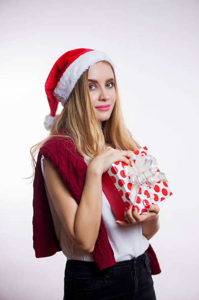 Happy pretty young woman in red Santa hat holding gift box on white background and looking at the camera. Christmas, new year and celebration concept - Fotoğraf, Görsel