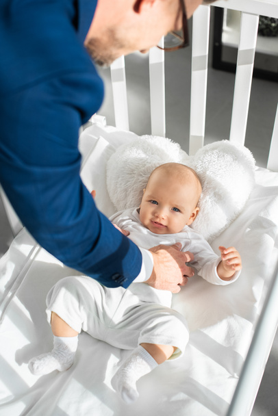 cropped view of father in suit putting infant daughter into baby crib  - Photo, Image