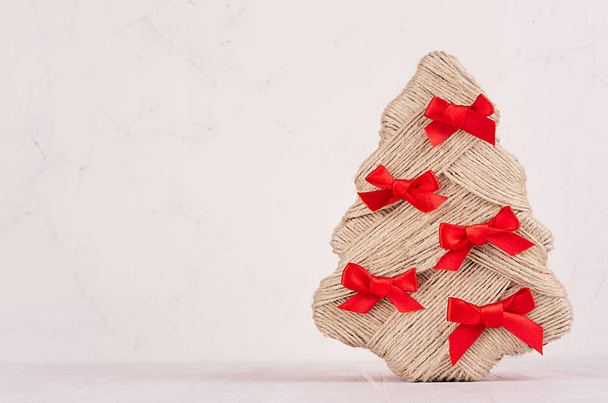 Christmas background - handmade New Year tree of jute with red ribbons on light white wooden board with copy space.  - Zdjęcie, obraz