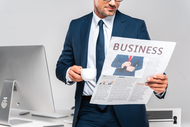 imagen recortada de empresario sosteniendo taza de café y leyendo periódico de negocios aislado en blanco
 - Foto, Imagen