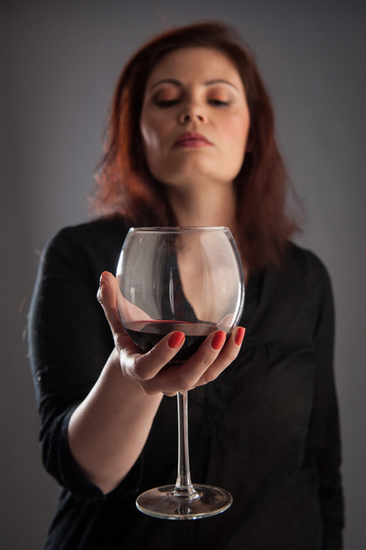 Женщина с бокалом красного вина в руке на сером фоне. Мелкая глубина резкости
. - Фото, изображение