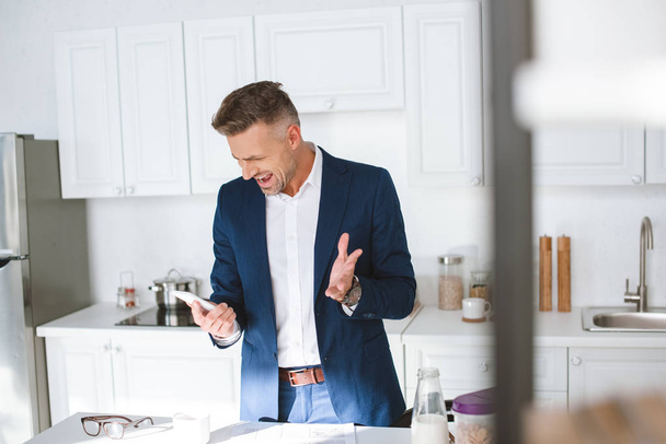 valikoiva painopiste vihainen liikemies huutaa pitäen älypuhelin keittiössä
 - Valokuva, kuva
