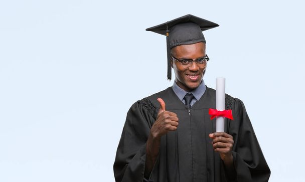 Young graduated african american man holding degree over isolated background happy with big smile doing ok sign, thumb up with fingers, excellent sign - Foto, Bild