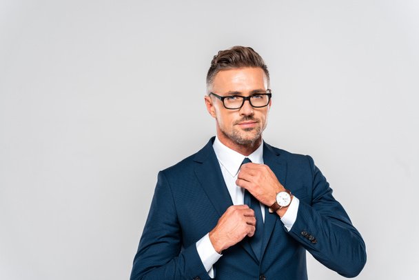 portrait of handsome businessman in suit and glasses tying tie isolated on white - 写真・画像