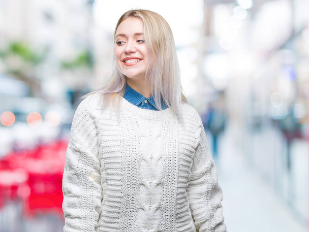 Nuori blondi nainen yllään talvi villapaita yli eristetty tausta etsii pois puolelta hymyillen kasvot, luonnollinen ilme. Nauraen itsevarmana
. - Valokuva, kuva