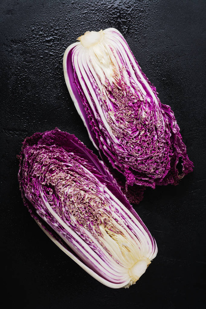 Fresh raw purple Chinese cabbage cut in half on a black concrete old background. Top view. - Foto, Imagem