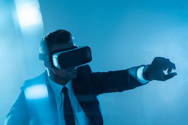 businessman in virtual reality headset touching something isolated on blue, artificial intelligence concept - Photo, Image