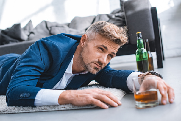 selective focus of drunk businessman lying on carpet near glass with alcohol drink - Φωτογραφία, εικόνα