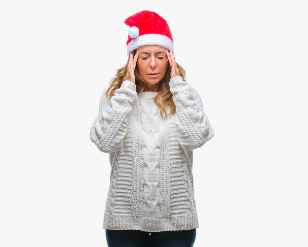 Mujer hispana mayor de mediana edad que usa sombrero de Navidad sobre fondo aislado con la mano en la cabeza para el dolor en la cabeza porque el estrés. Dolor de migraña
. - Foto, imagen