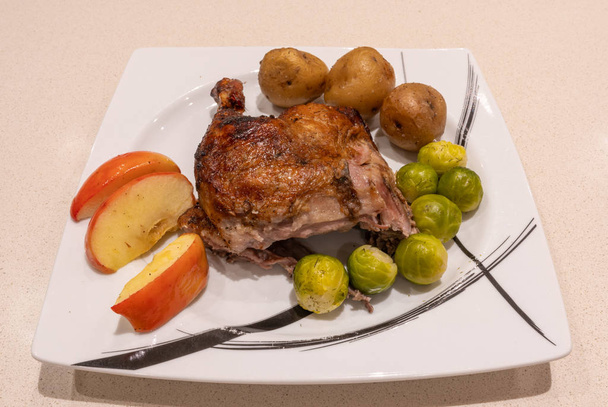 Jambe d'oie rôtie et croustillante sur l'assiette avec pommes de terre rôties, pommes et choux de Bruxelles
. - Photo, image