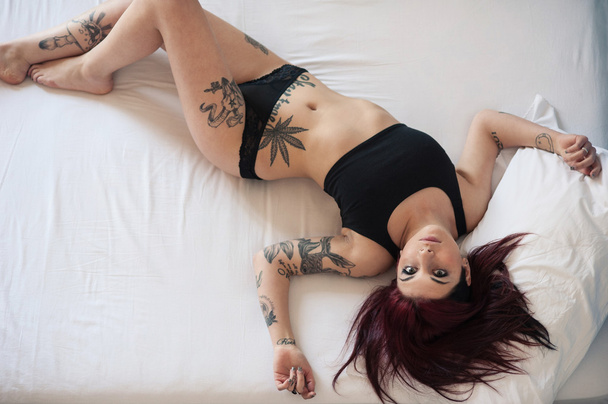 Sensual portrait of beautiful girl with tattoo lying on bed. - Photo, image