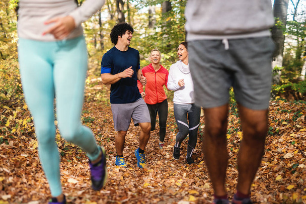 Piccolo gruppo di amici felici che corrono nel bosco in autunno vestiti in abbigliamento sportivo
. - Foto, immagini
