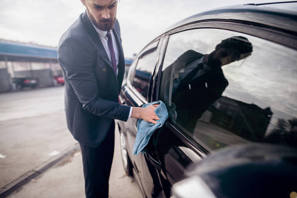 przystojny młody stylowe Brodaty mężczyzna w garniturze, czyszczenie samochodu z mikrofibry o mycia samoobsługowa stacja obsługi samochodów - Zdjęcie, obraz