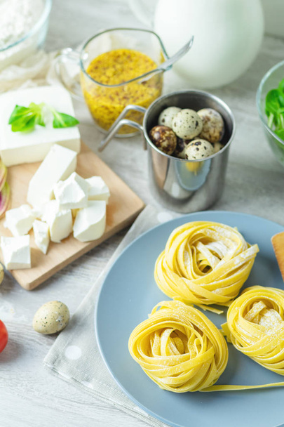 RAW σπιτικά ζυμαρικά Ιταλικά τυπικό Λινγκουίνι noodles σε πιάτο, τα αυγά ορτυκιού, πράσινο μαρούλι, ντομάτες, γαλλική μουστάρδα, φέτα. Κάτοψη, εσωτερικη. - Φωτογραφία, εικόνα
