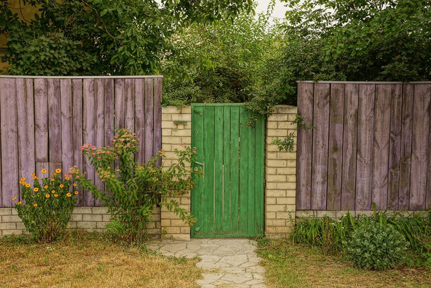 onderdeel van een landelijke houten hek en een gesloten groene deur in het gras en takken - Foto, afbeelding