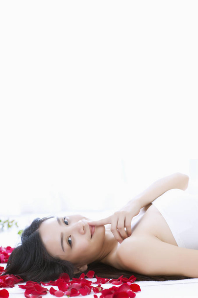 Young Asian woman lying on the bed with roses and looking at the camera, - Foto, Imagem