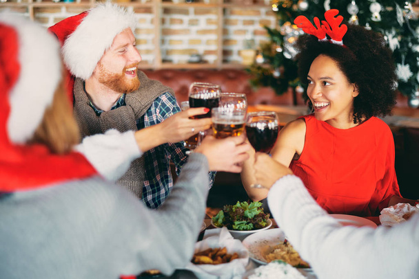 Friends drinking alcohol and having dinner for Christmas eve at home. Christmas holidays concept. - Photo, Image