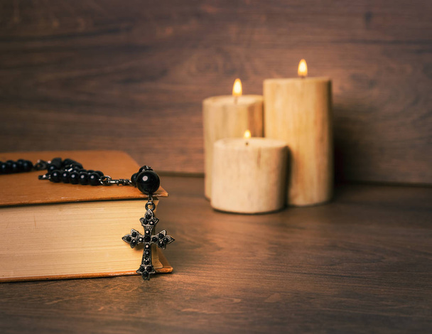 Black rosary and cross on the Bible at wooden table,background candle. Religion at school.vintage style. - Photo, Image