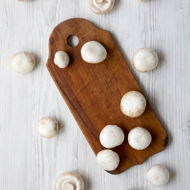 Cogumelos champignon em tábua de madeira sobre fundo de madeira branco, vista aérea. De cima, deitado plano
. - Foto, Imagem