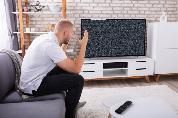 Frustrated Young Man Sitting On Sofa Near Television With No Signal - 写真・画像