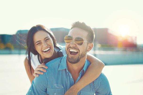 Feliz joven pareja de moda riendo a cuestas posan al aire libre
 - Foto, Imagen