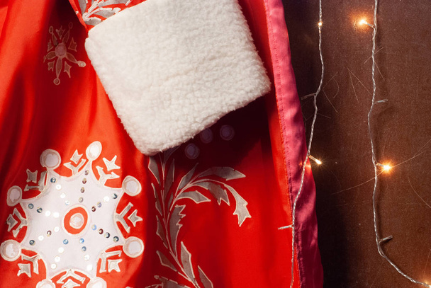 Nahaufnahme von rotem Weihnachtsmann-Pelzmantel, Weihnachtsmannkleidung und Girlanden, Hintergrund zum neuen Jahr, - Foto, Bild