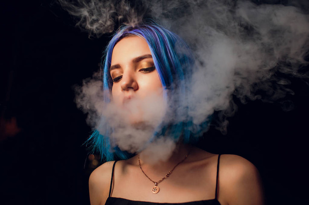 young woman smoking electronic cigarette against a black background - 写真・画像