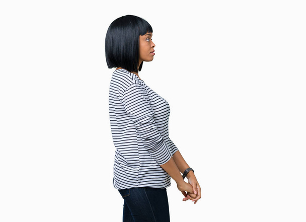 Beautiful young african american woman wearing stripes sweater over isolated background looking to side, relax profile pose with natural face with confident smile. - Photo, image
