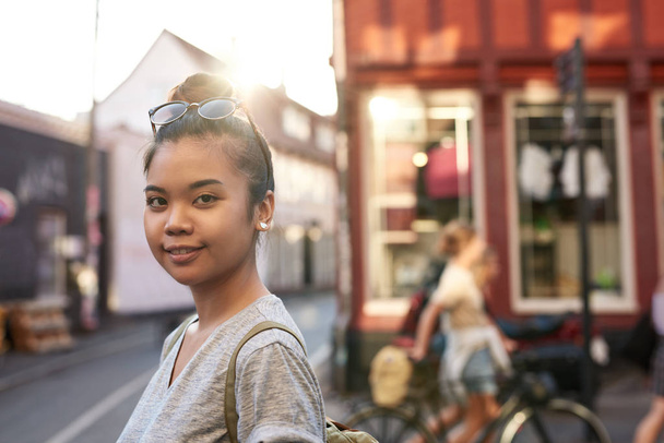 Portrait of a casually dressed young Asian woman smiling while walking along city streets in the late afternoon - Foto, afbeelding