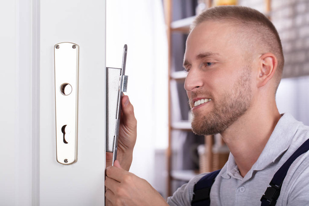Close-up Of A Smiling Young Man Fixing Door Lock In House - 写真・画像