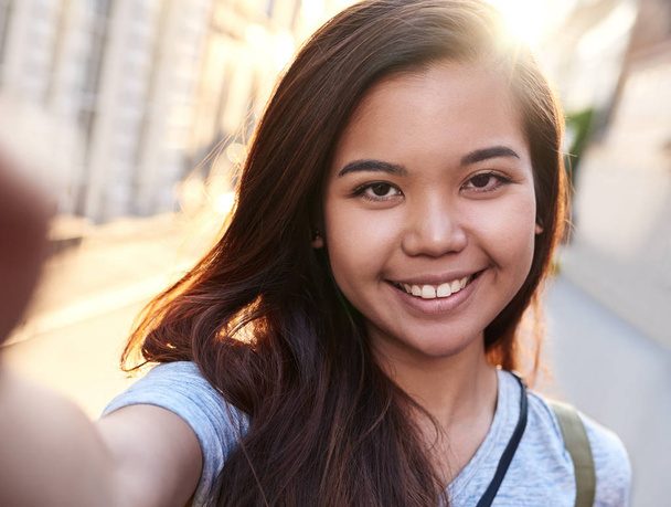 Close up portrait of a joyful young Asian woman taking a selfie with her cellphone while exploring the city on foot - Foto, afbeelding