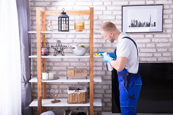 Vue de côté d'un jeune homme concierge nettoyage étagère dans la maison
 - Photo, image