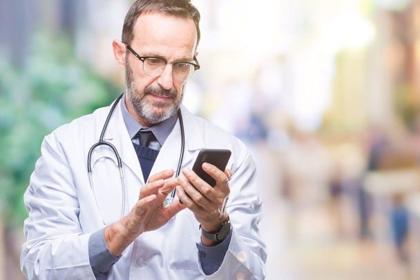 Старший лікар середнього віку використовує смартфон на ізольованому фоні з впевненим виразом на розумному обличчі мислення серйозно
 - Фото, зображення